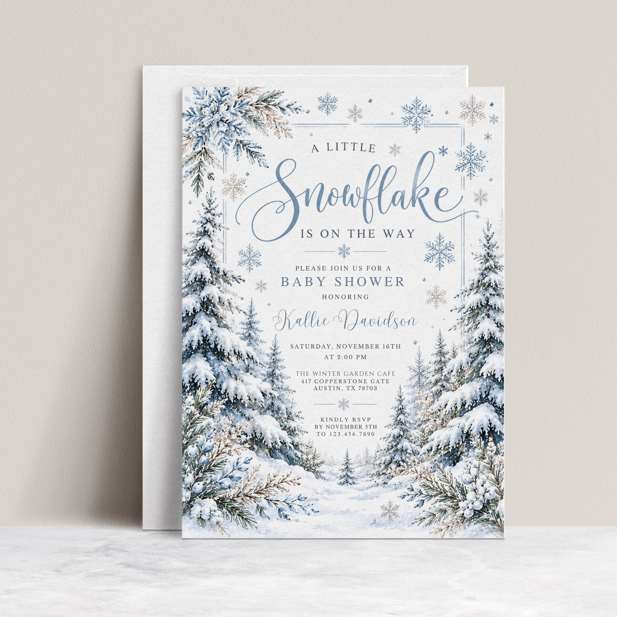 Winter baby shower invitation with blue snowflakes, snow-covered evergreen trees, frosted foliage, and A Little Snowflake Is on the Way wording on white