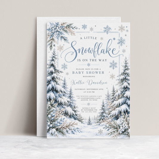Winter baby shower invitation with blue snowflakes, snow-covered evergreen trees, frosted foliage, and A Little Snowflake Is on the Way wording on white
