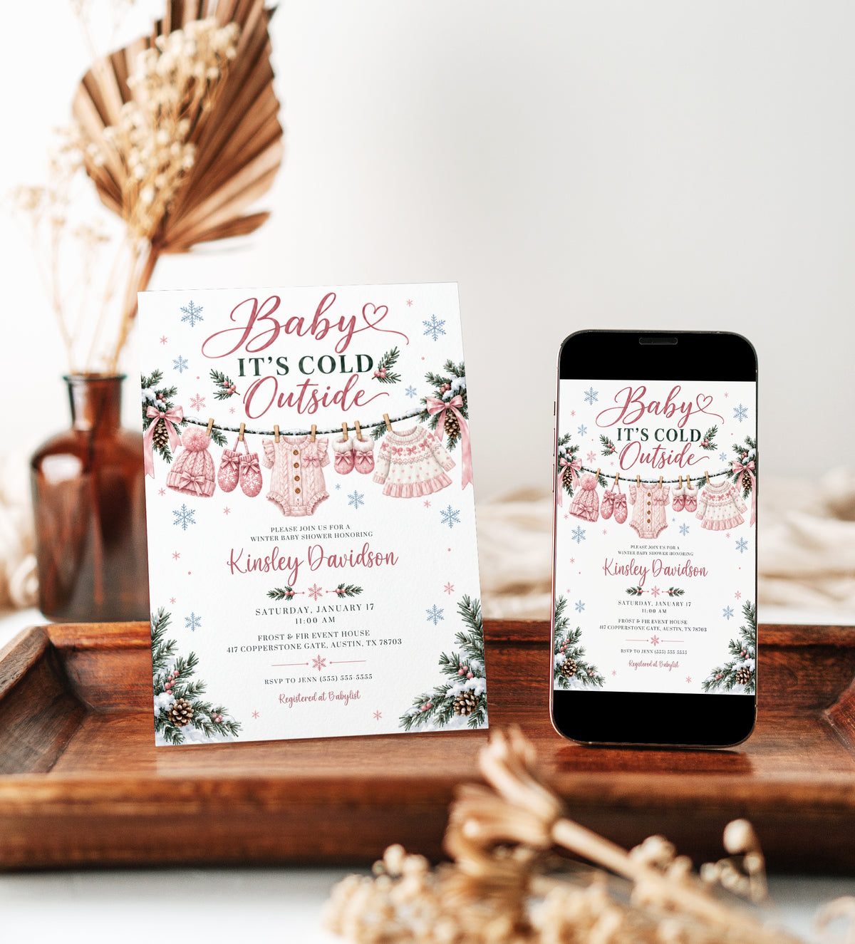 Baby It’s Cold Outside baby shower invitation with pink knit baby clothes, snowflakes, pink bows, pine branches, pinecones, and winter baby girl shower details