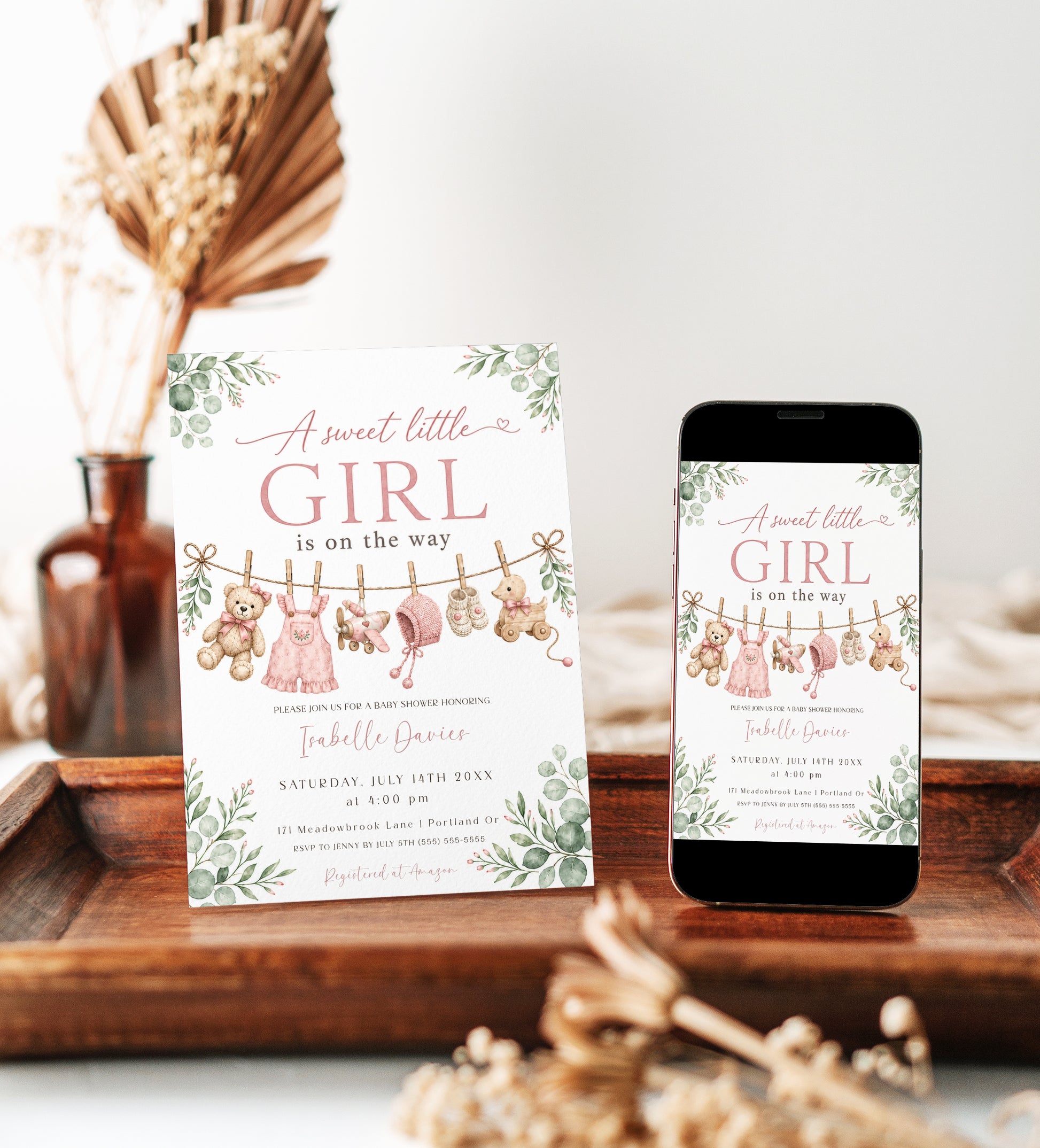Sweet little girl baby shower invitation with hanging baby clothes, a teddy bear, and greenery in soft pink and sage