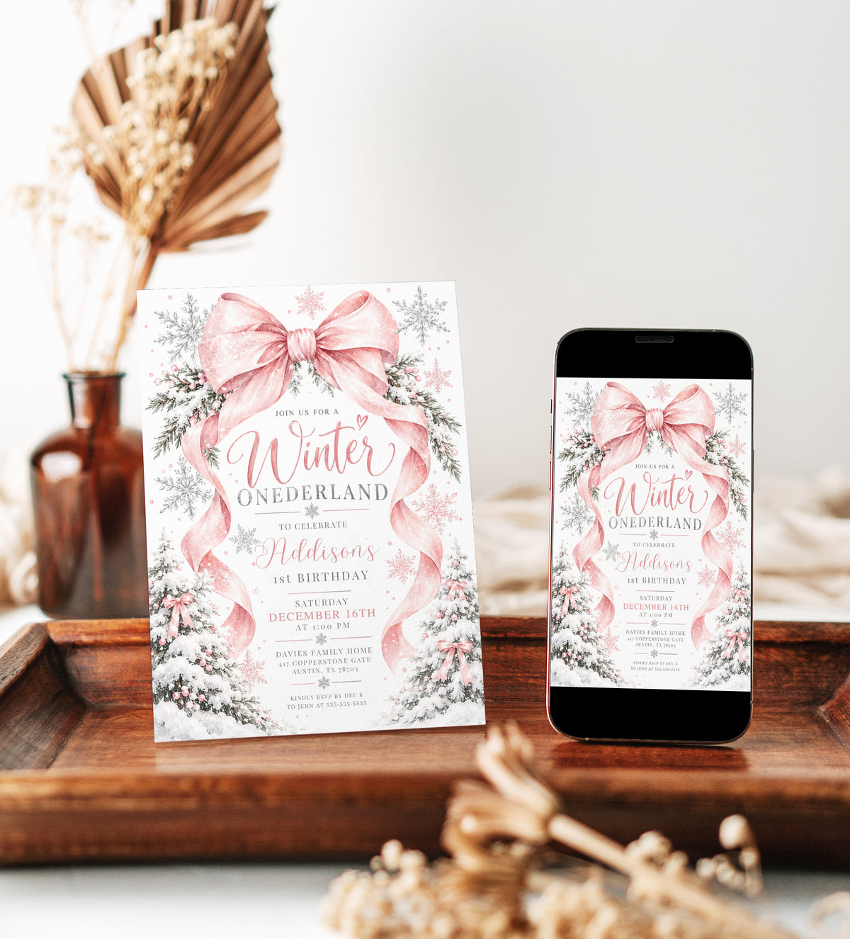 Winter Onederland 1st birthday invitation with a large pink bow, flowing ribbons, silver and pink snowflakes, and snow-covered trees decorated with pink bows