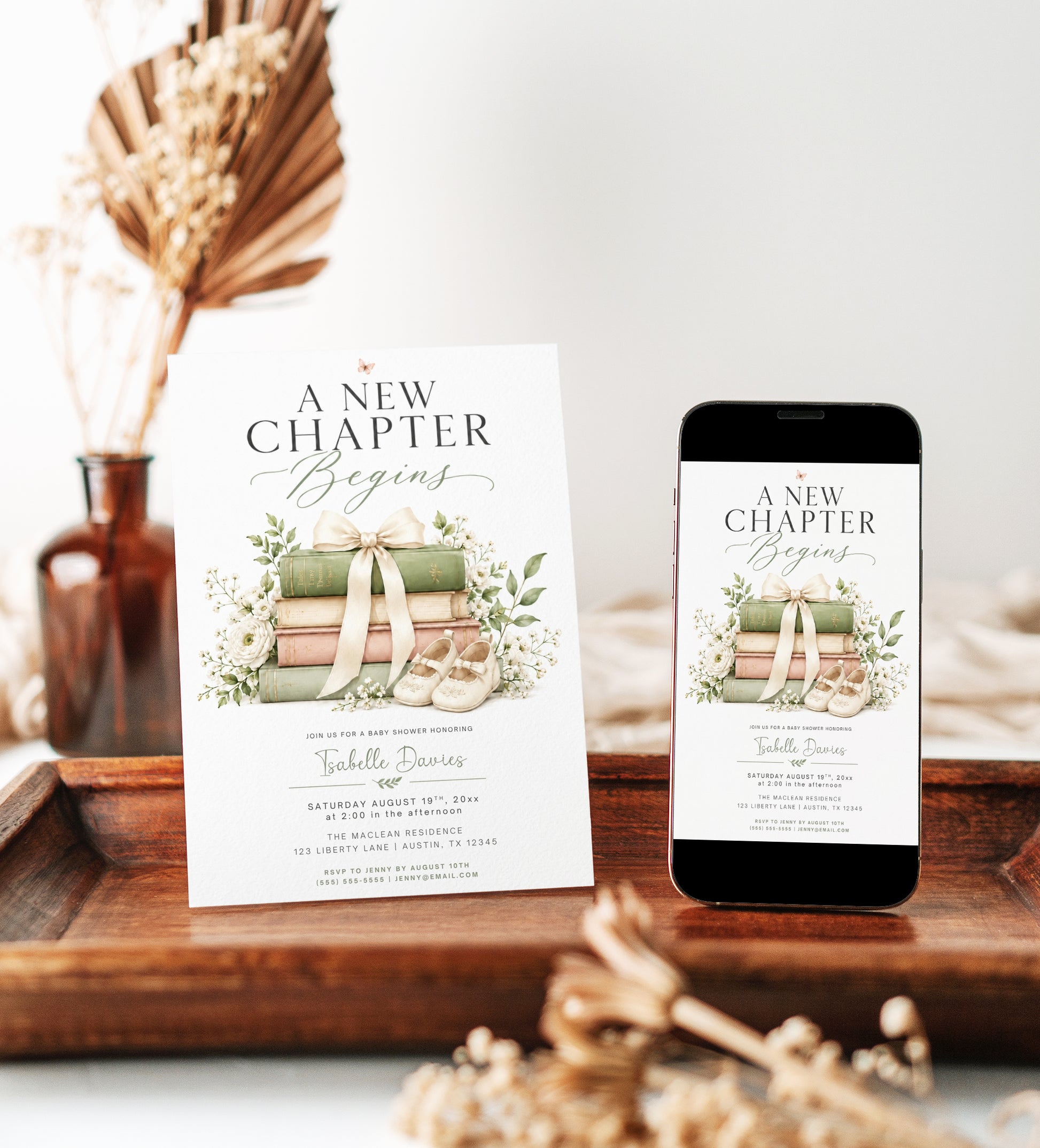 Editable a new chapter baby shower invitation Canva template with stacked vintage hardcover books tied with cream bow, baby shoes, white ranunculus, baby's breath, and botanical greenery on a white background