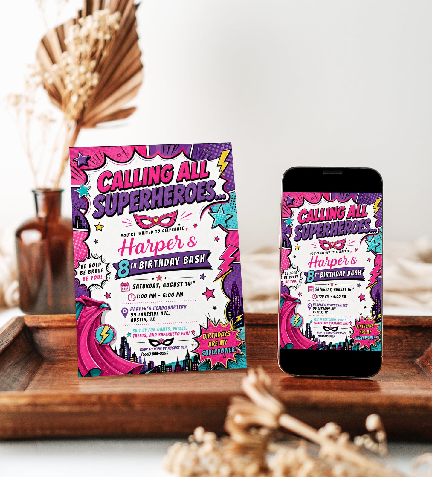 Girls superhero birthday invitation featuring a pink comic book design with cape, mask, city skyline, stars, lightning bolts and bold action graphics.
