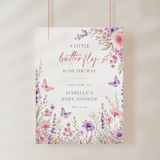 Editable butterfly baby shower welcome sign Canva template with watercolour pink and purple butterflies, peonies, lavender, and wildflower meadow on a white background, shown as a hanging print mockup