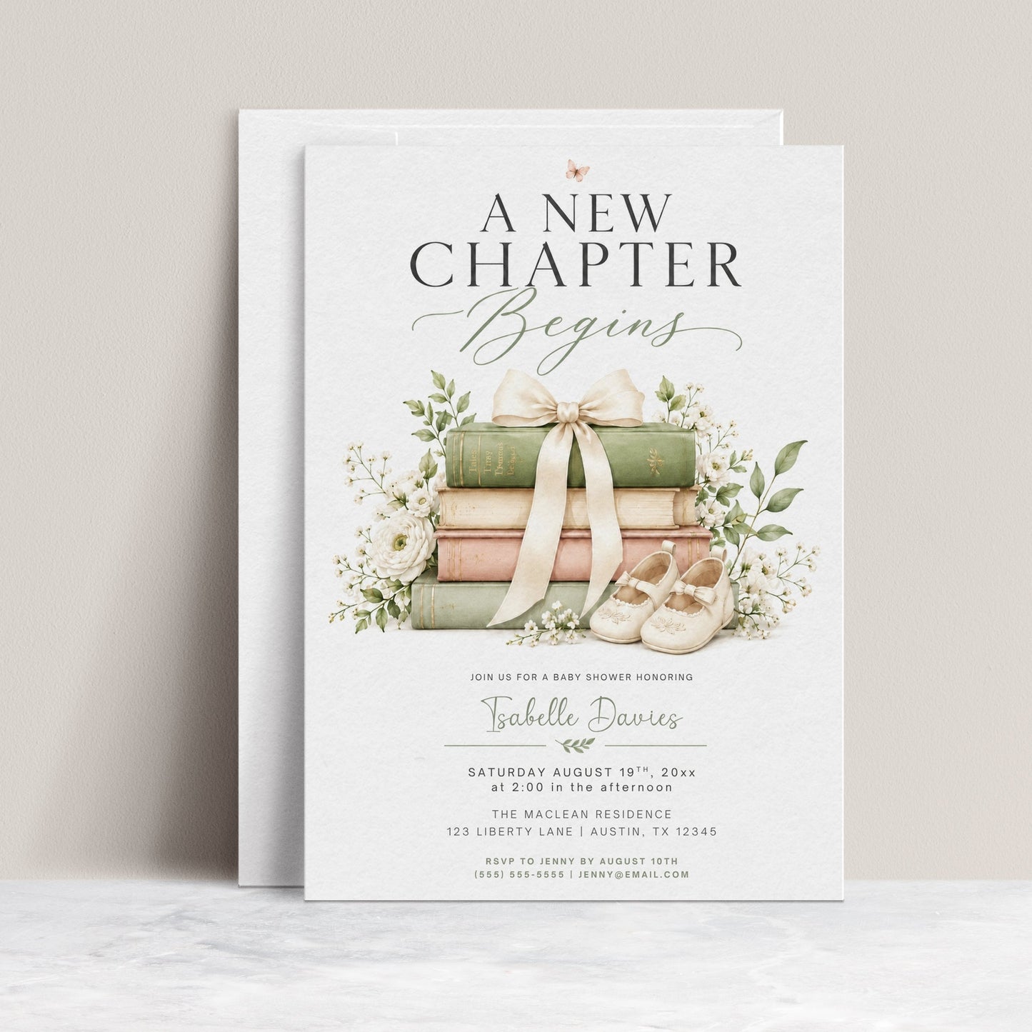 Editable a new chapter baby shower invitation Canva template with stacked vintage hardcover books tied with cream bow, baby shoes, white ranunculus, baby's breath, and botanical greenery on a white background