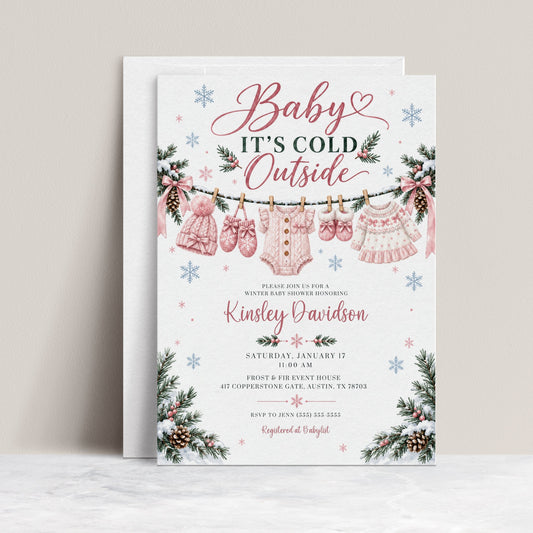 Baby It’s Cold Outside baby shower invitation with pink knit baby clothes, snowflakes, pink bows, pine branches, pinecones, and winter baby girl shower details