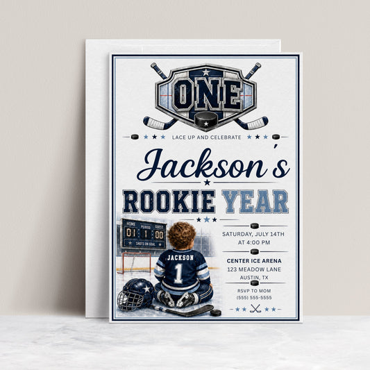 Rookie Year first birthday invitation with little hockey player, ice rink, scoreboard, helmet, hockey sticks, puck, and navy blue birthday party details