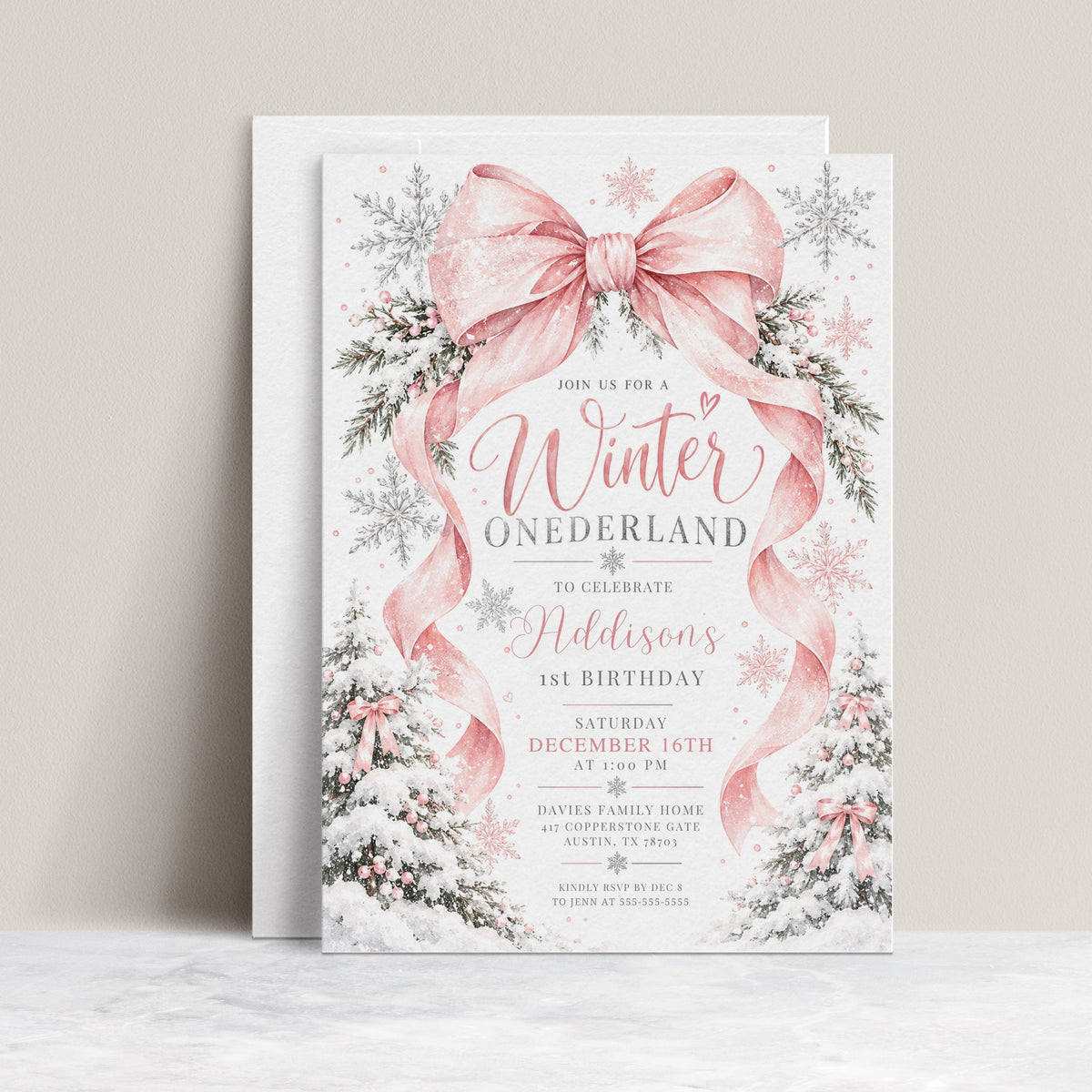 Winter Onederland 1st birthday invitation with a large pink bow, flowing ribbons, silver and pink snowflakes, and snow-covered trees decorated with pink bows