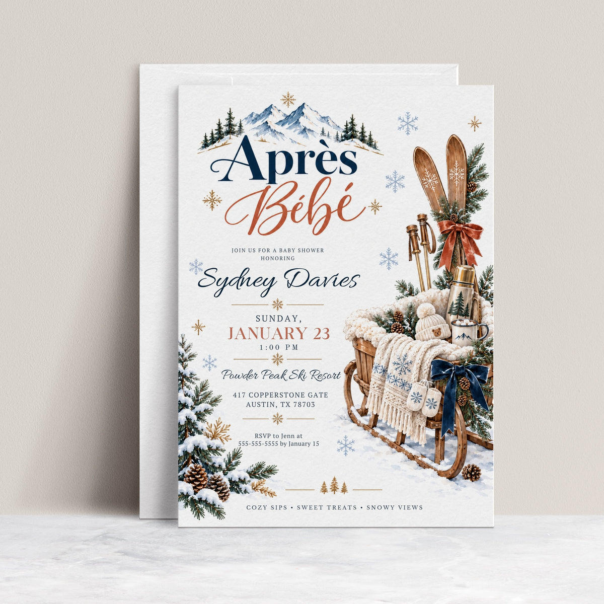 Après Bébé baby shower invitation with wooden skis, a rustic sled, knit baby hat and mittens, hot cocoa, snowy mountains, and evergreen branches
