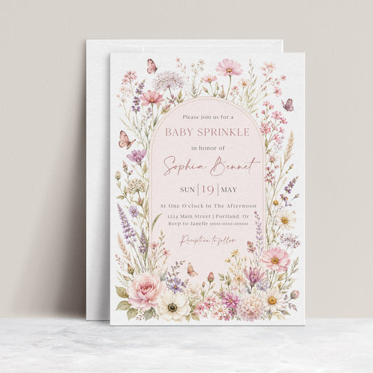 Editable wildflower baby sprinkle invitation Canva template with watercolour botanicals, blush arch, butterfly details, and script typography on a soft pink background