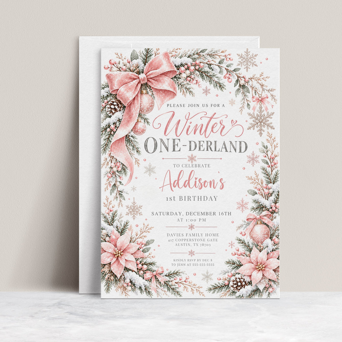 Winter Onederland 1st birthday invitation with a large pink bow, pink poinsettias, snow-covered greenery, pinecones, pink ornaments, and delicate snowflakes