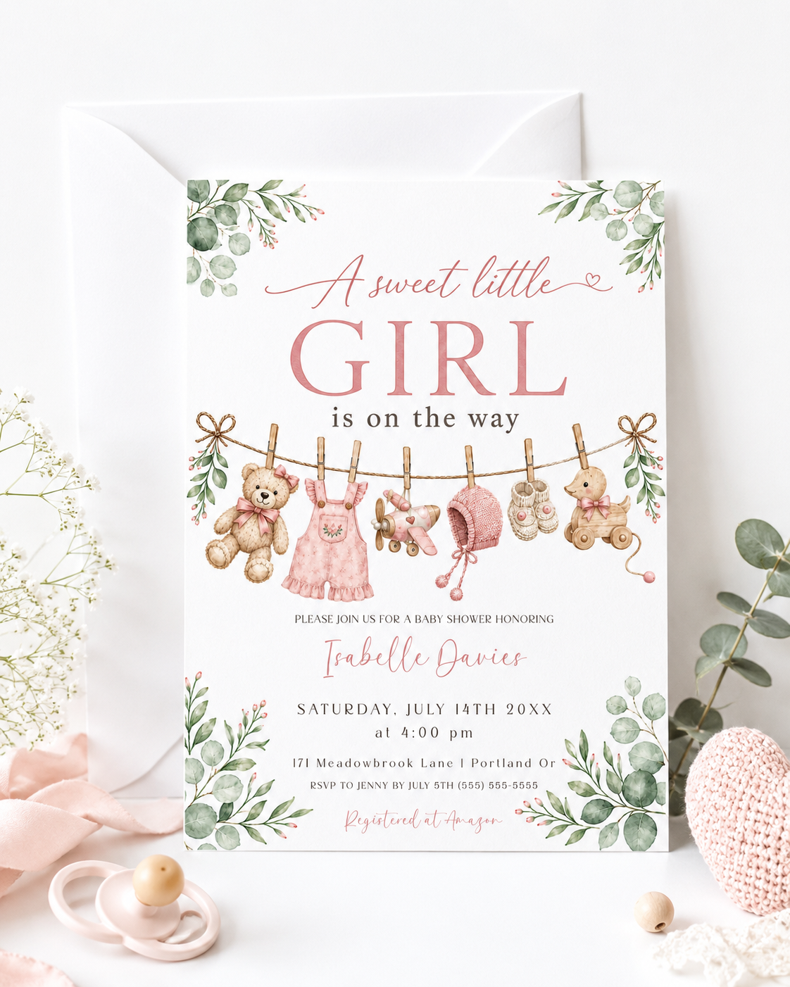 Sweet little girl baby shower invitation with hanging baby clothes, a teddy bear, and greenery in soft pink and sage